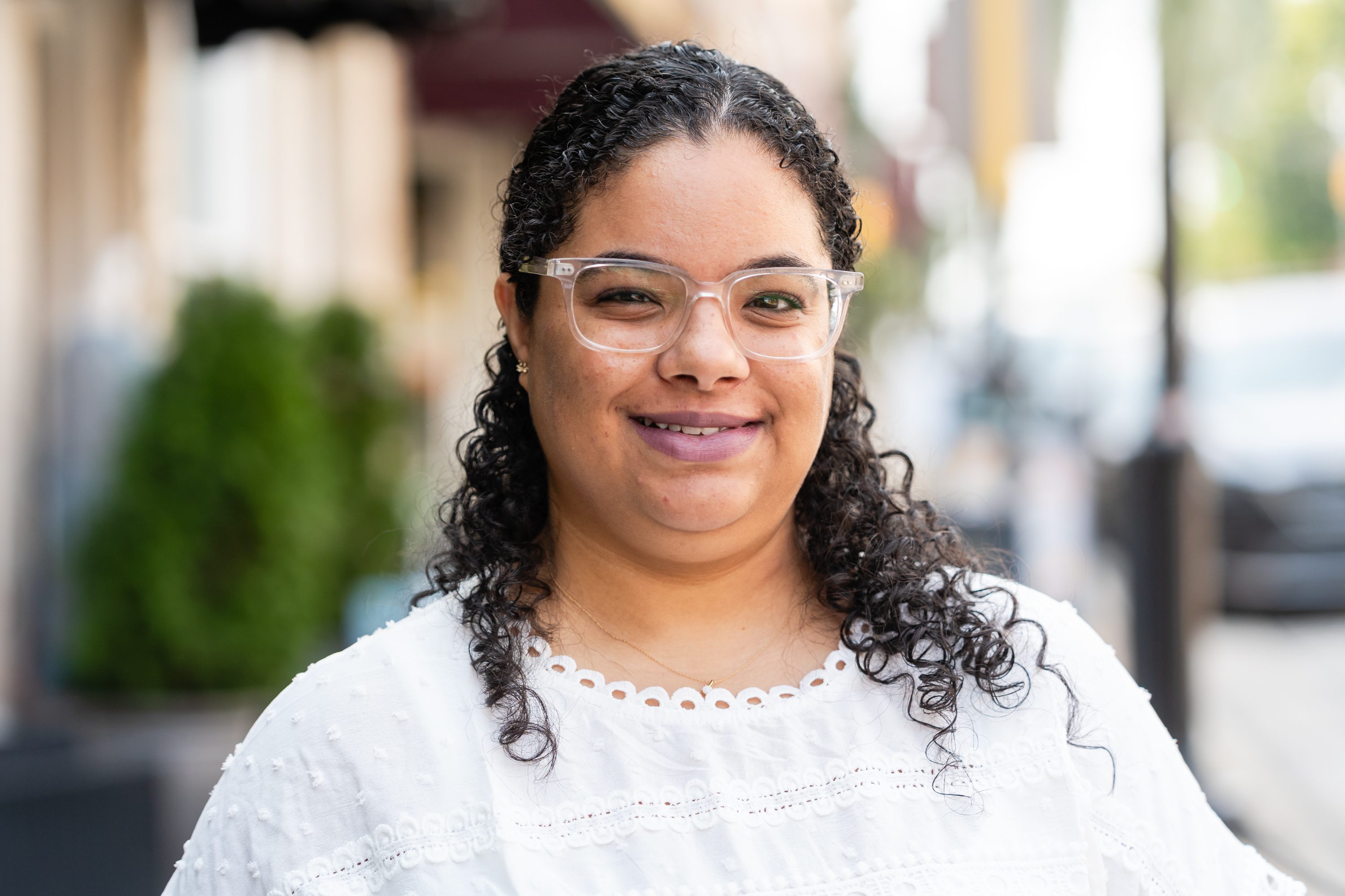 A woman with curly hair wearing glasses and white shirt.