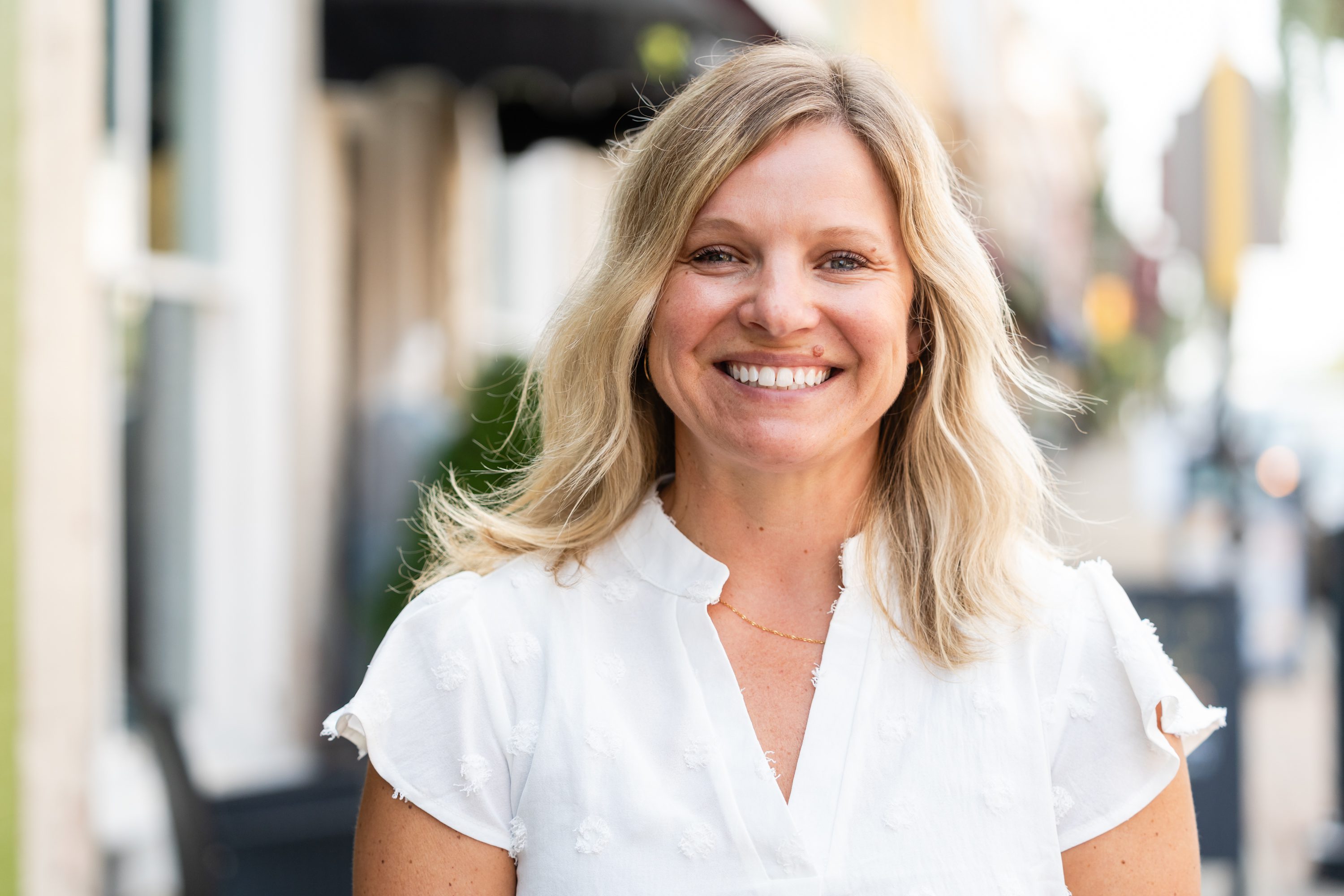 A woman smiling for the camera in front of some buildings.