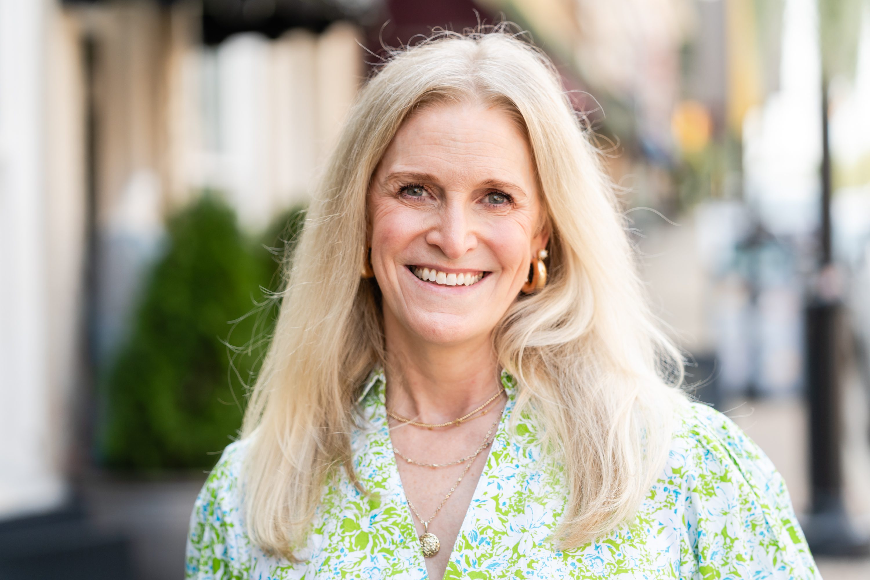 A woman with long blonde hair wearing a green floral shirt.