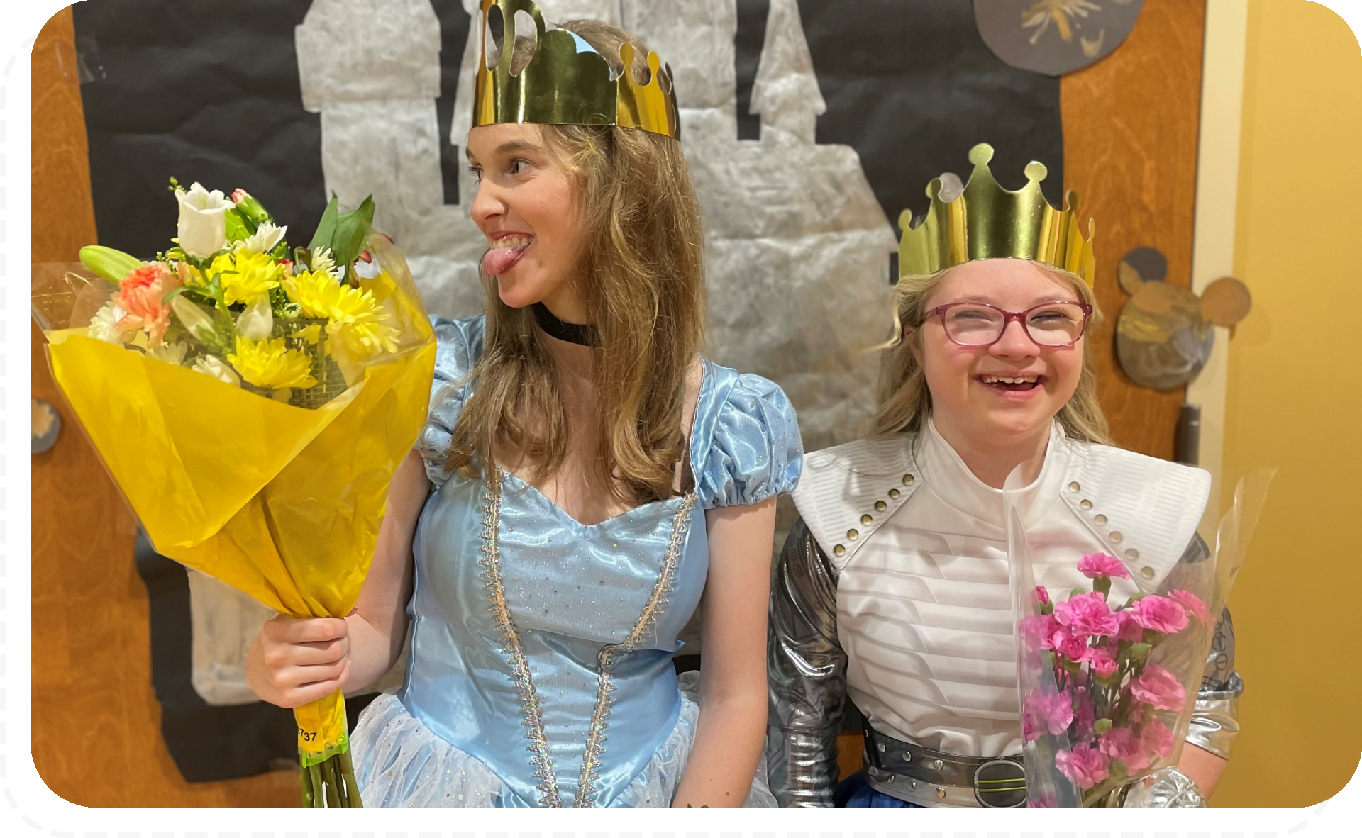 Two women in costumes holding flowers and smiling.