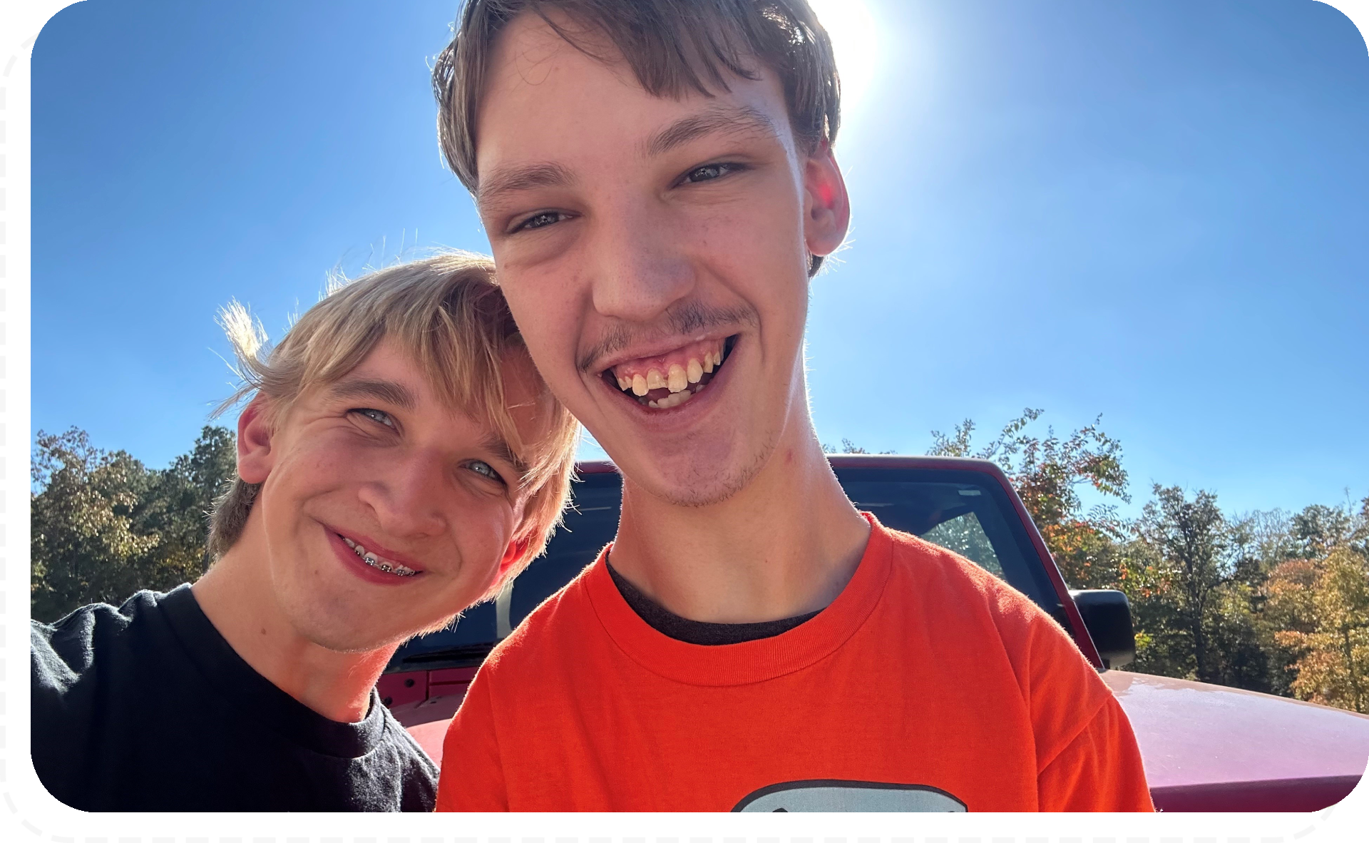 Two boys smiling for a picture in front of the sun.